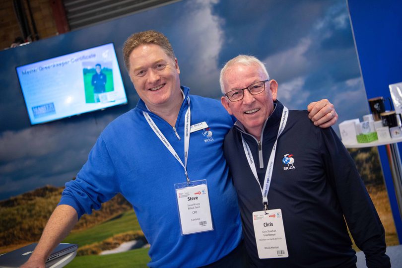 Two men wearing delegate badges standing together at an event stand at Harrogate Convention Centre