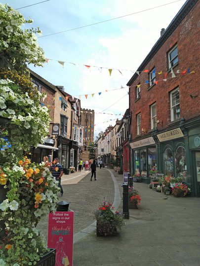 Shop-lined winding cobbled street with a cathedral towards the end