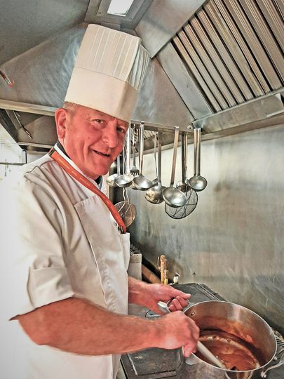 A chef in a white hat stirring a large pot filled with delicious food.