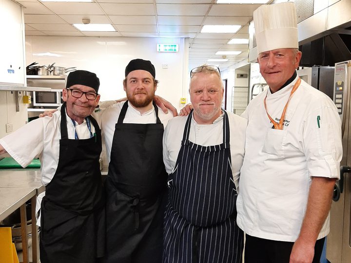 Four chefs happily posing for a photo in a kitchen.
