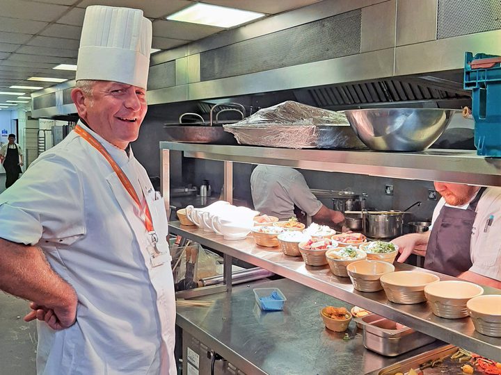 Chef standing near counter filled with fresh ingredients.